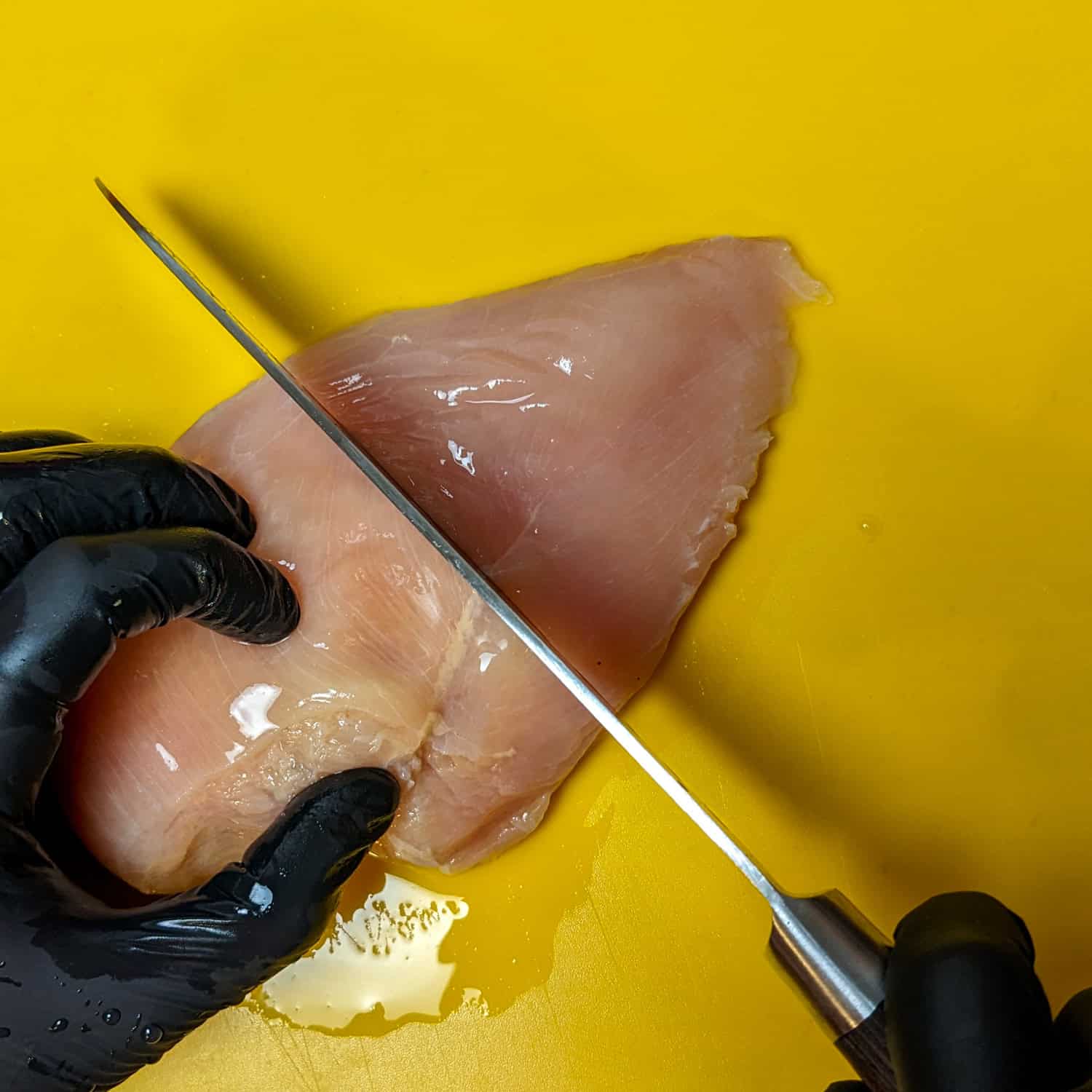 Chicken breast being sliced in half widthwise.